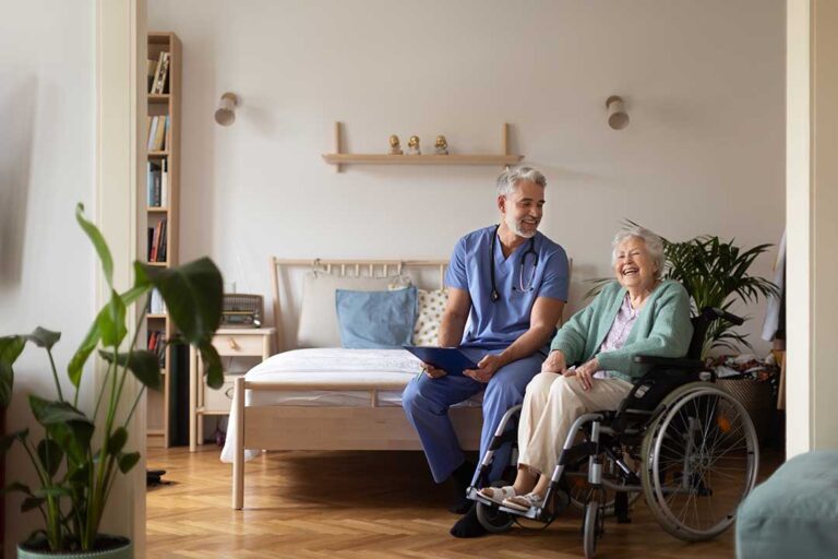 A caregiver helping an older adult walk down a hallway decorated with cheerful art and natural light.