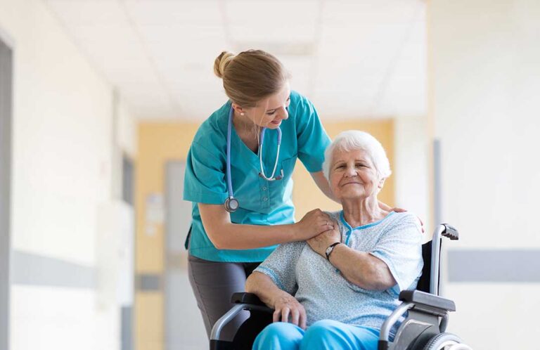 A group of seniors sitting together in a communal living room, talking and smiling with a staff member nearby.
